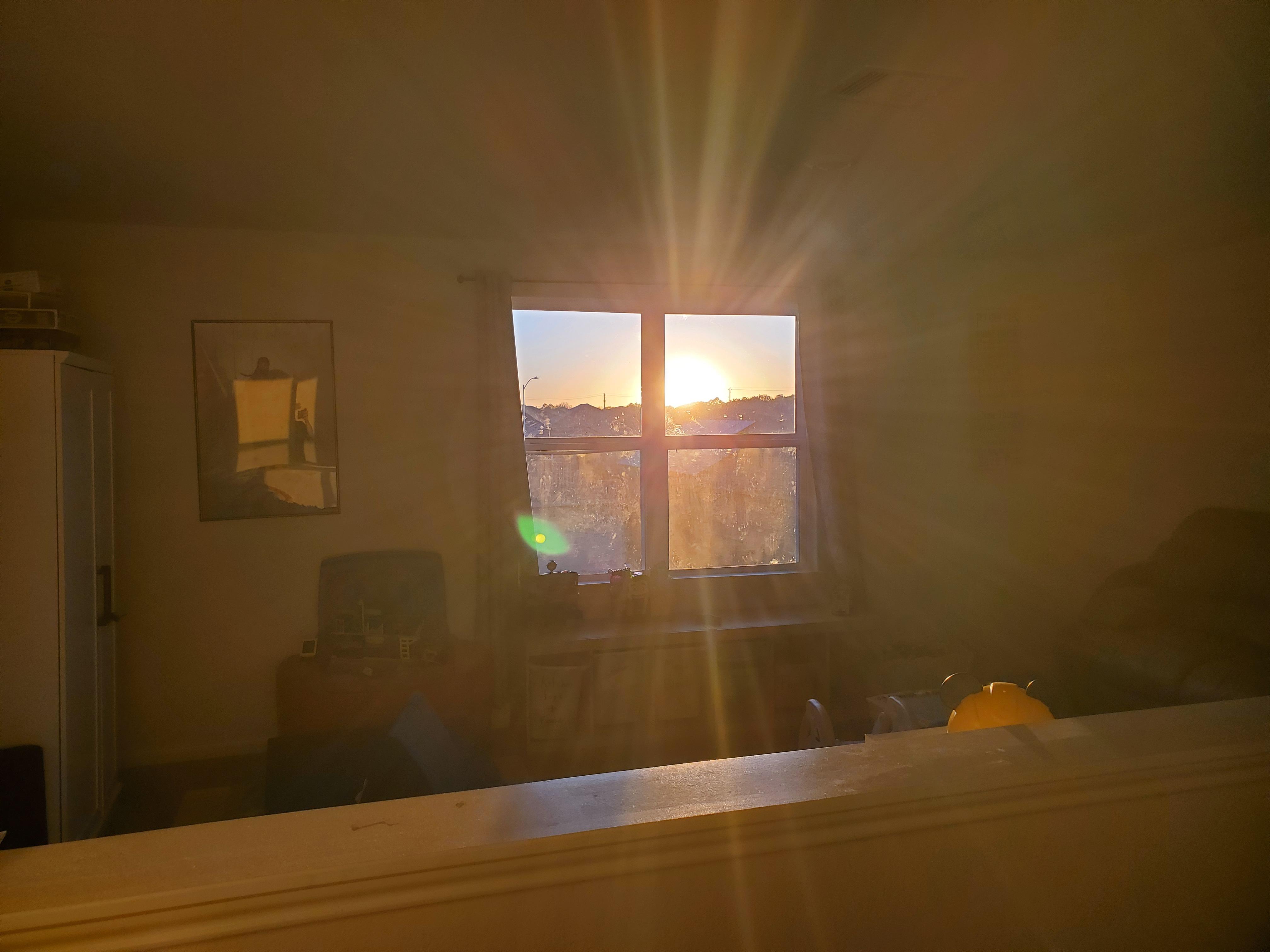 A sunset, as seen through a second floor window. The bright orange light radiates, illuminating the walls and all around it