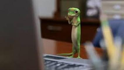 The Geico gecko standing in front of a computer