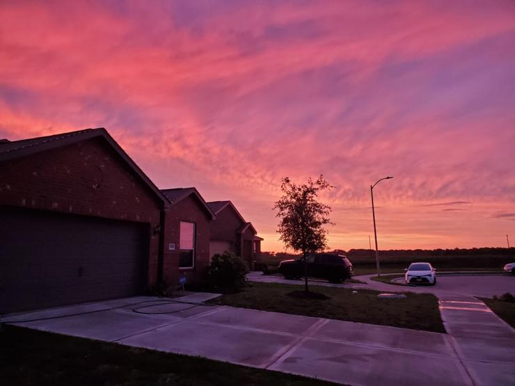 A cul-de-sac with a couple houses and cars visible. There are cirrus clouds visible, shining pink against a purple-ish blue sky. The houses are dark purple, reflecting the light of the setting sun.