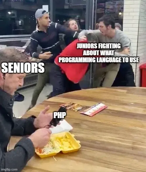 Fight inside a restaurant/diner. Background group of 3-4 men fighting with the words "Juniors fighting about what programming language to use". A man in the foreground calming eating marked "Seniors" reading his phone marked "PHP".