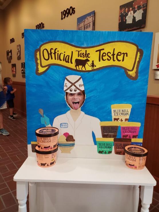 Young teen girl with face in cutout of old fashioned ice cream man. Cartons of Blue Bell Ice Cream below her.