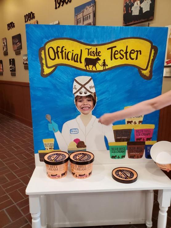 Young boy with face in cutout of old fashioned ice cream man. Cartons of Blue Bell Ice Cream sit nearby.