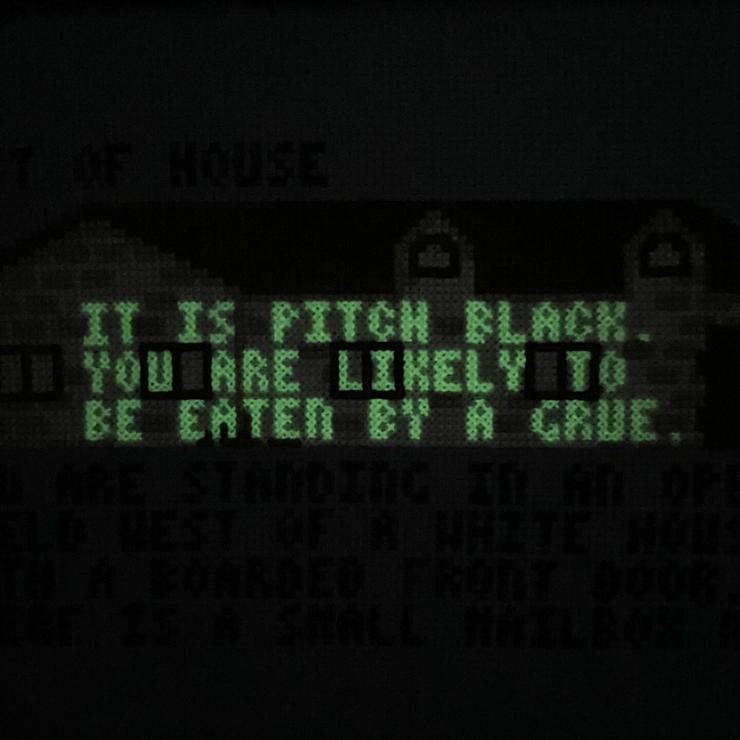 Zoomed-in “West of House” cross stitch in total darkness, the house and original text gone. In green glowing letters: “IT IS PITCH BLACK. YOU ARE LIKELY TO BE EATEN BY A GRUE.”