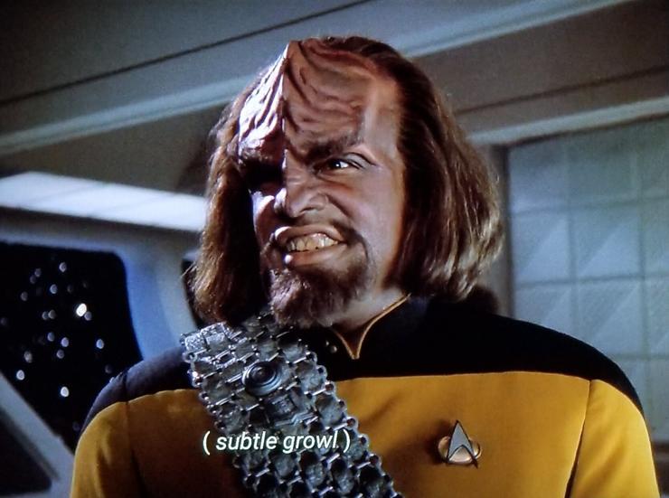 Worf is standing in ten forward on the Enterprise. (TNG era) He's pictured up close, and has a weird and crazed hungry or horny or maybe both hungry *and* horny Klingon smile on his face. His lip is curled up a bit, showing his teeth. Closed caption reads, "(subtle growl)"