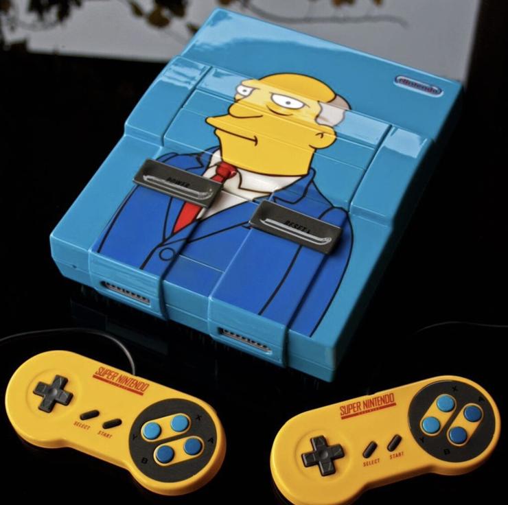 A blue SNES with an image of Superintendent Chalmers on it and yellow controllers. 