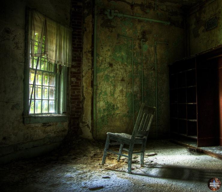 A room dimly lit by a window on the wall. In front of the window is a wooden chair. Its front leg is lifting upward as though reaching toward the window