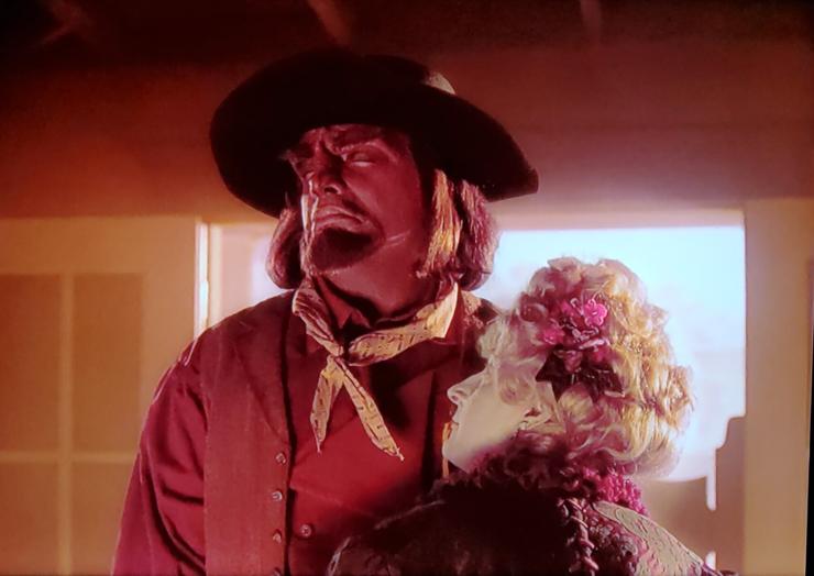 Old western looking scene here, dusty air, saloon doors. Worf is pictured looking up with eyes closed. He's dressed as a cowboy with hat and handkerchief and everything. Standing and embracing Cowboy Worf is a fair maiden looking damsel, head held close against his Klingon chestal region. BUT WAIT, the fair maiden is Data. Data is wearing a big flowery wig full of red flowers and blond curls and wearing a nice fancy dress. No caption.