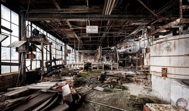 A vast room filled with vats and pipes. The floor is covered with moss, mold, and bits of machinery. A small sign hangs from the ceiling that reads "Quality And Pride Go Hand In Hand"