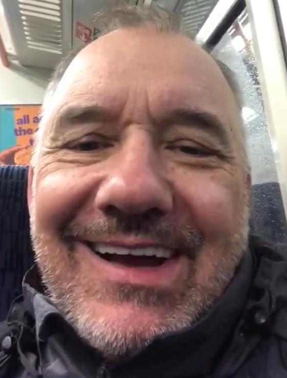 The incomparable Bob Mortimer as his business persona Train Guy. Here we see a closeup of a smiling older chap with a charming face and some stubble atop, as is below. He's sat on a train talking about kicking the goose upstairs into the business sky to see if it's feathers shake loose any success nuggets or something. 