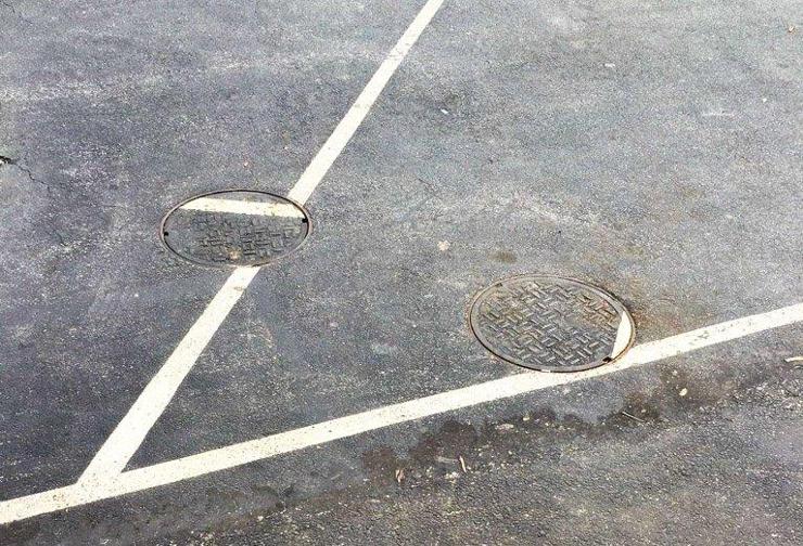 Twi manhole covers on white street lines embedded within asphalt. The lines on the covers are very misaligned with the street markings